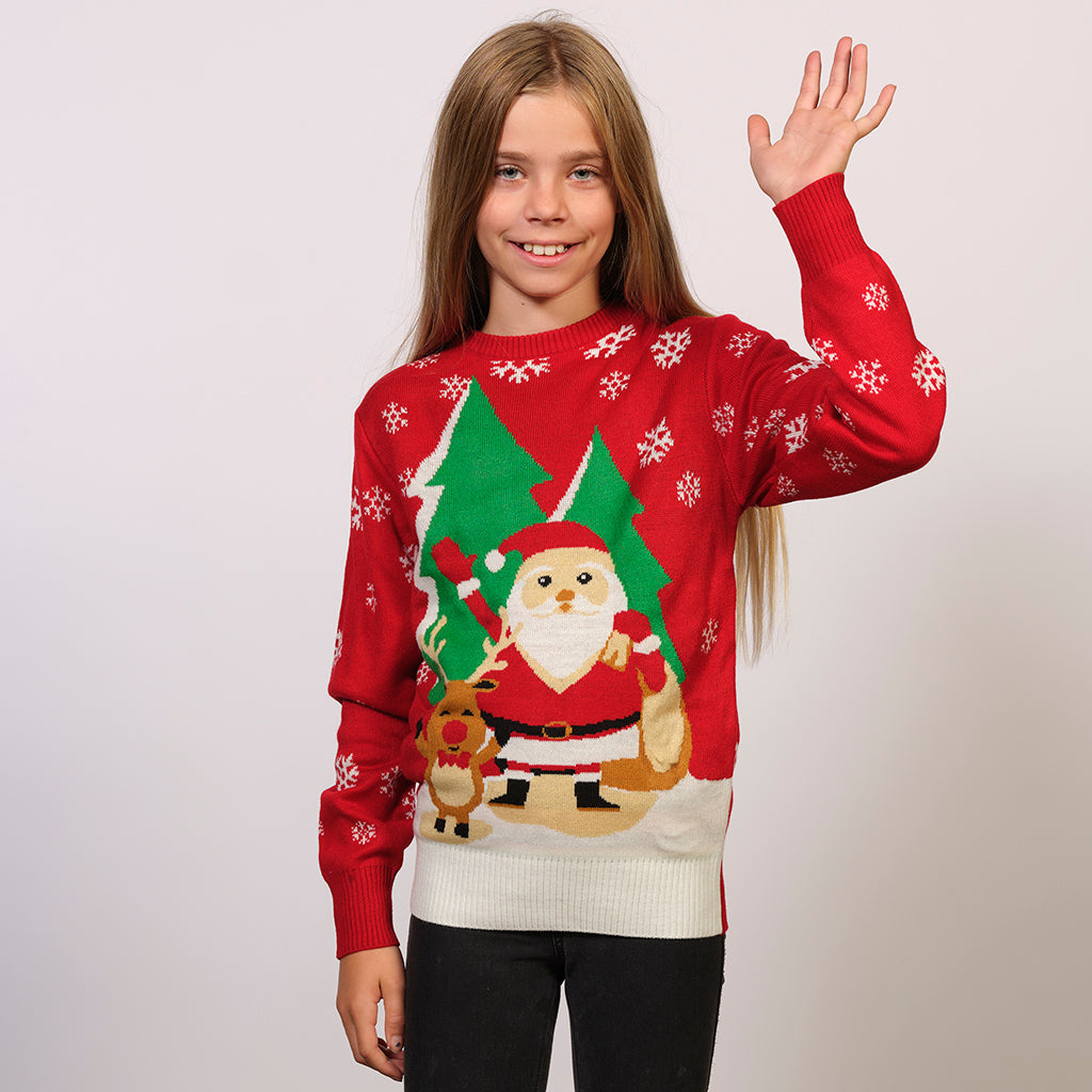 Et barn poserer iført en rød julegenser med julenissen og et reinsdyr på.