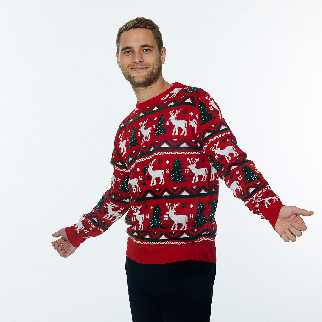 En mann har på seg en rød julegenser med reinsdyr og juletrær på.