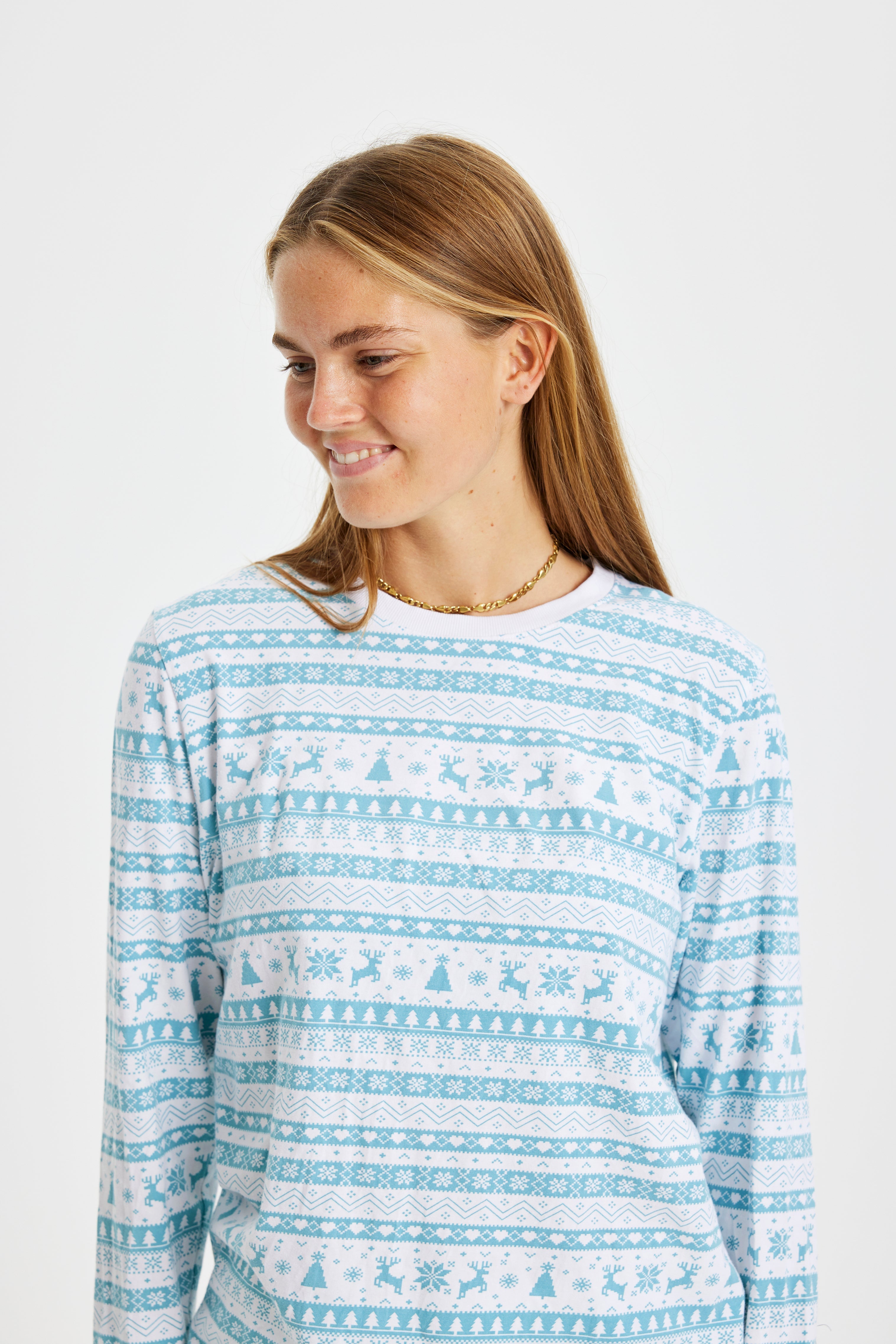 En smilende kvinne iført blå julepyjamas med julemønster.