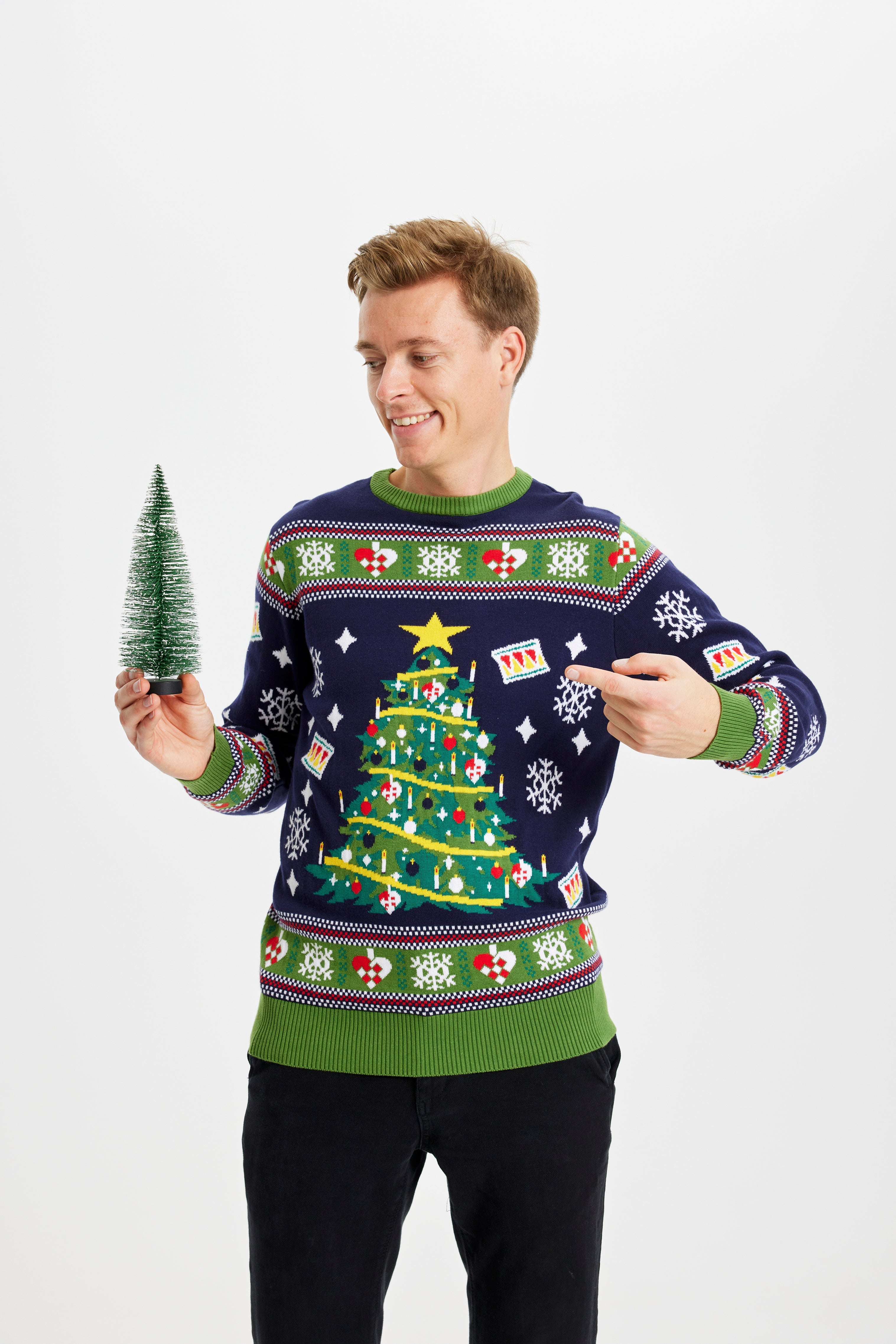 En mann med julepynt i hendene har på seg en julegenser med juletre og lys.