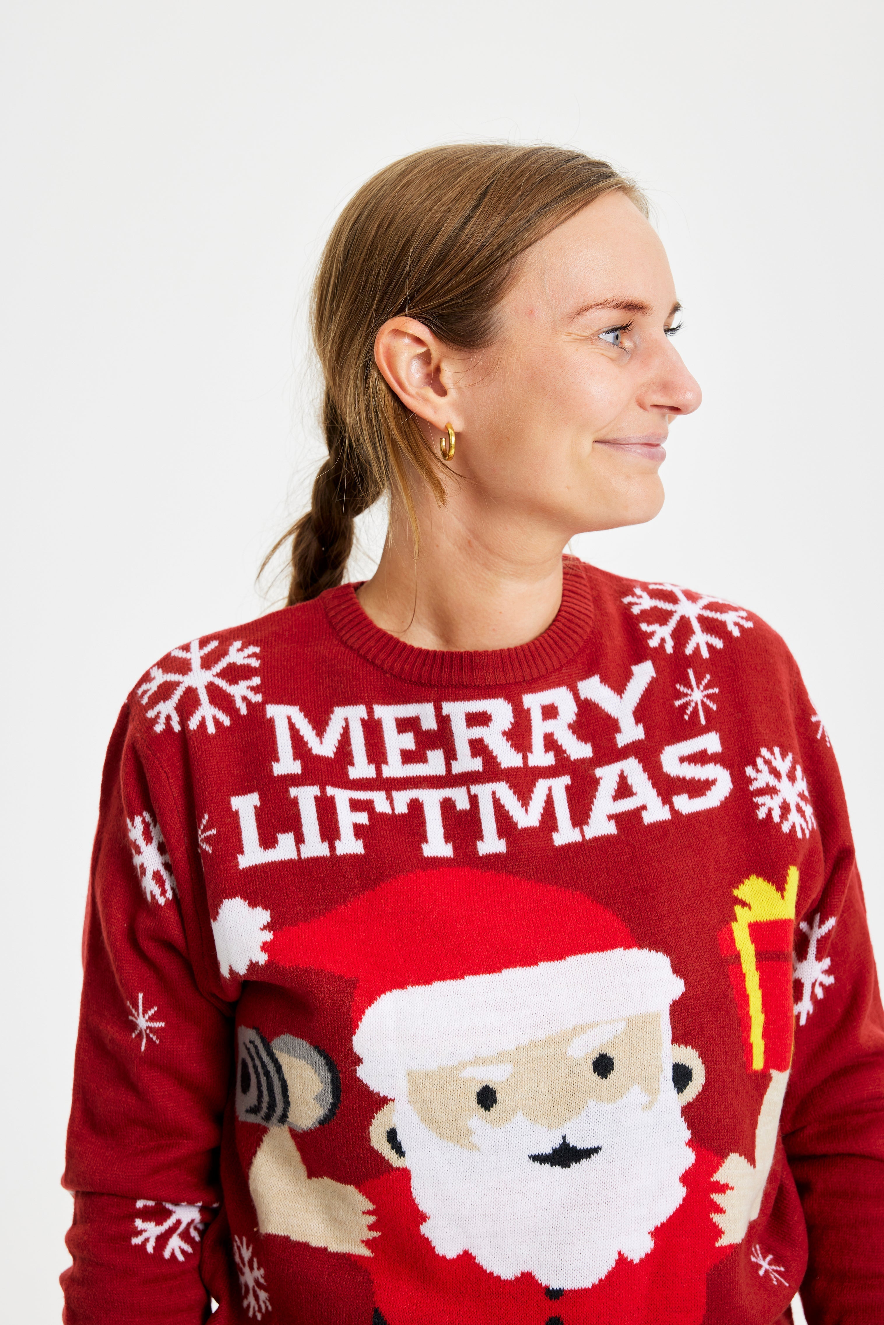 En smilende kvinne som ser til siden iført en rød julegenser med julenissen på.