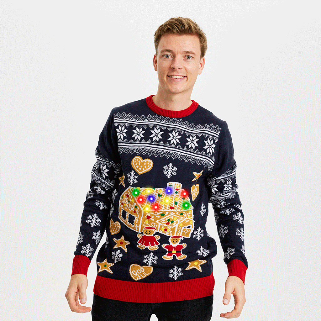 En mann iført julegenser med kakehus og lys.