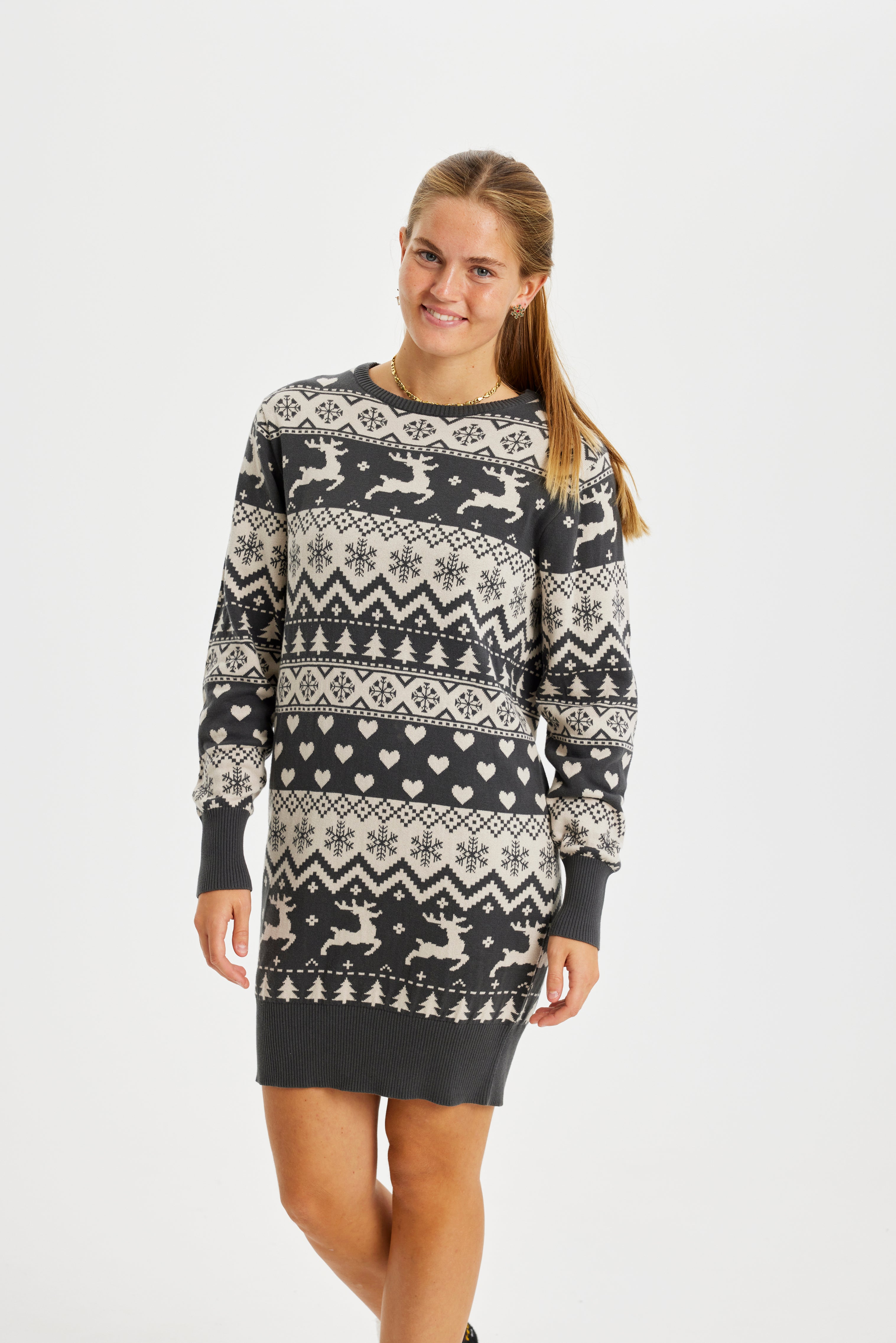 En smilende kvinne har på seg en strikket julekjole med reinsdyr på.