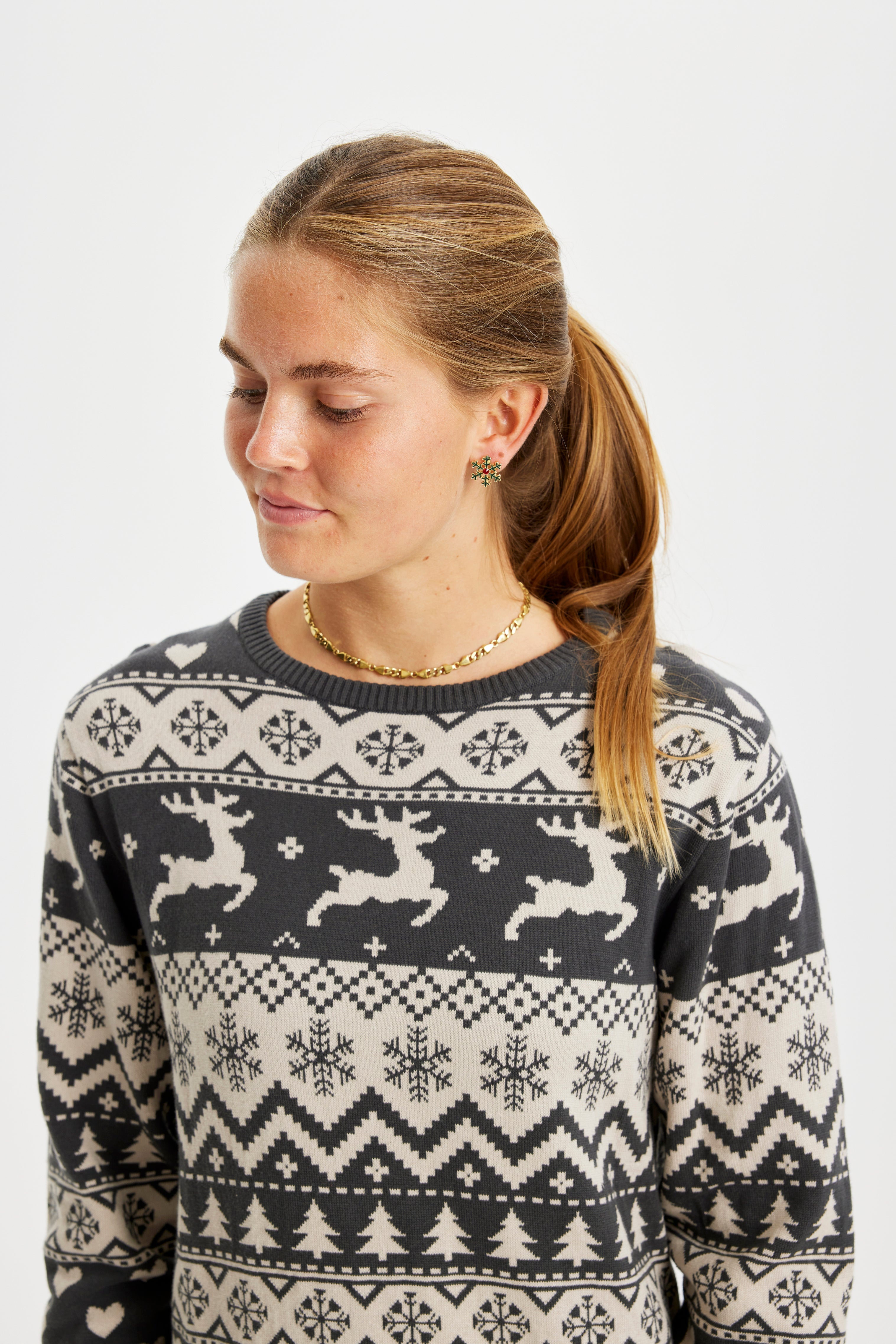 En kvinne ser til siden og har på seg en strikket julekjole med reinsdyr på.