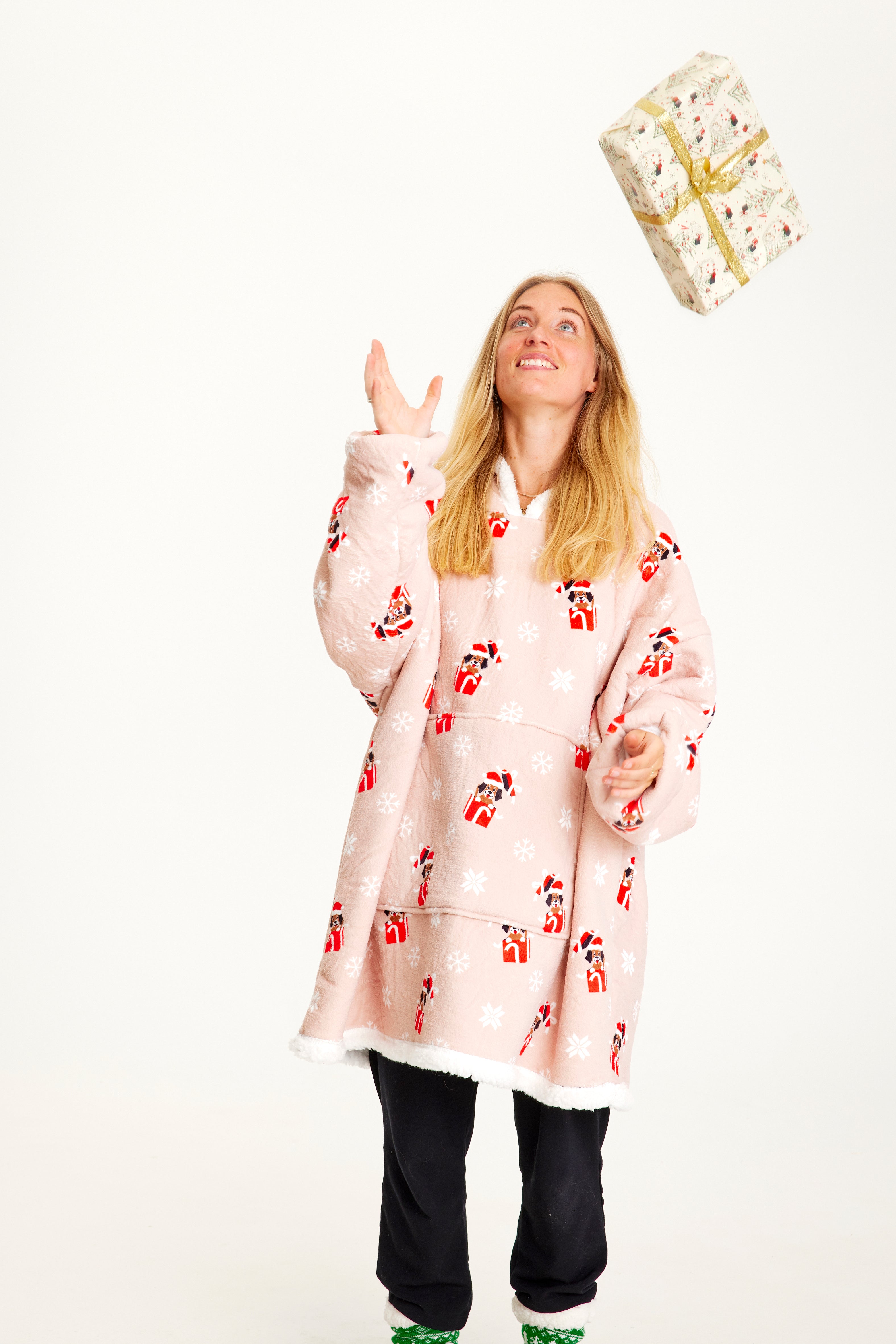 En kvinne med en gave iført en rosa julegenser med hunder på.