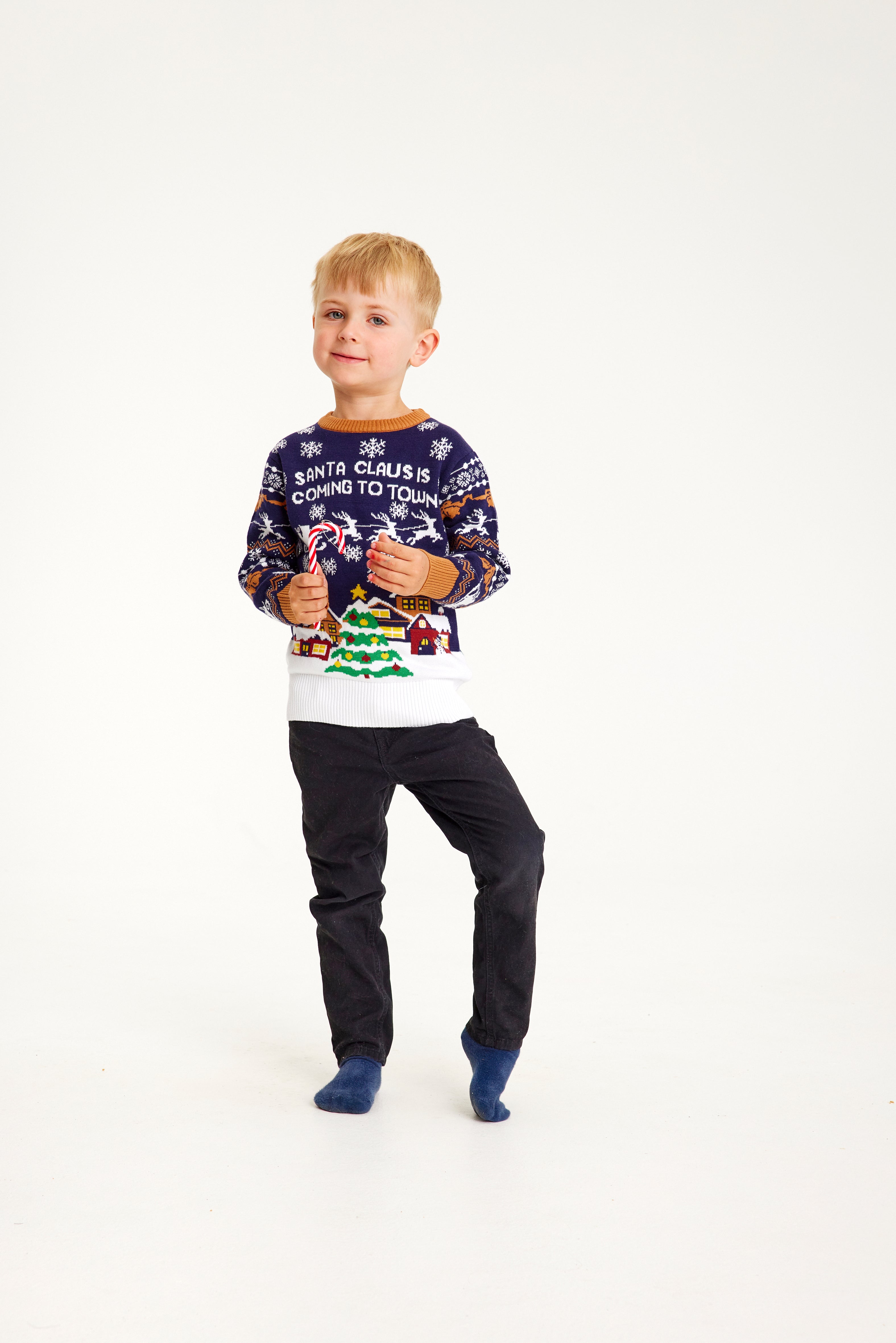 Et smilende barn med godteristokk og blå julegenser i et snødekt landskap.