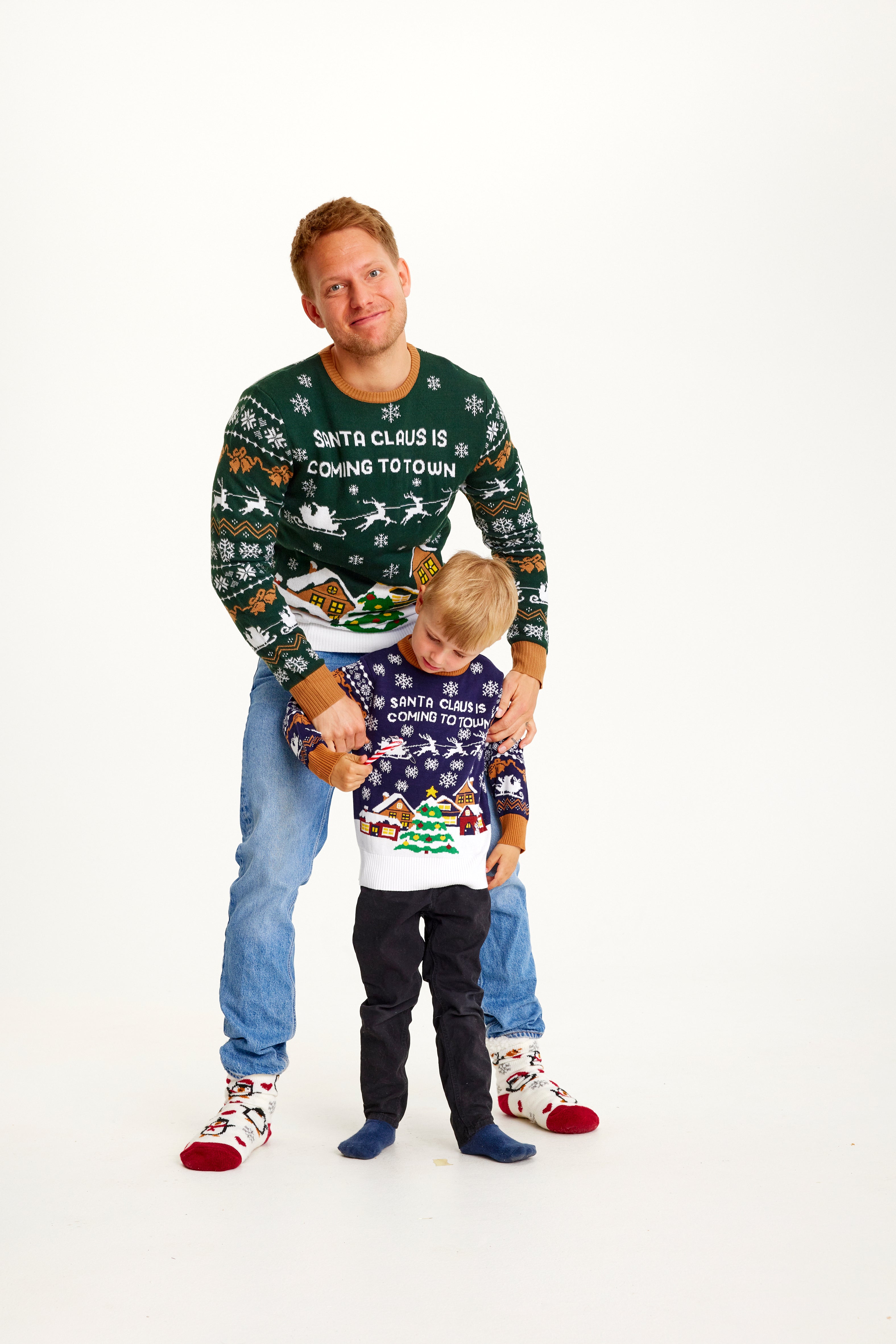 Et smilende barn og en mann iført julegensere i et snødekt landskap.