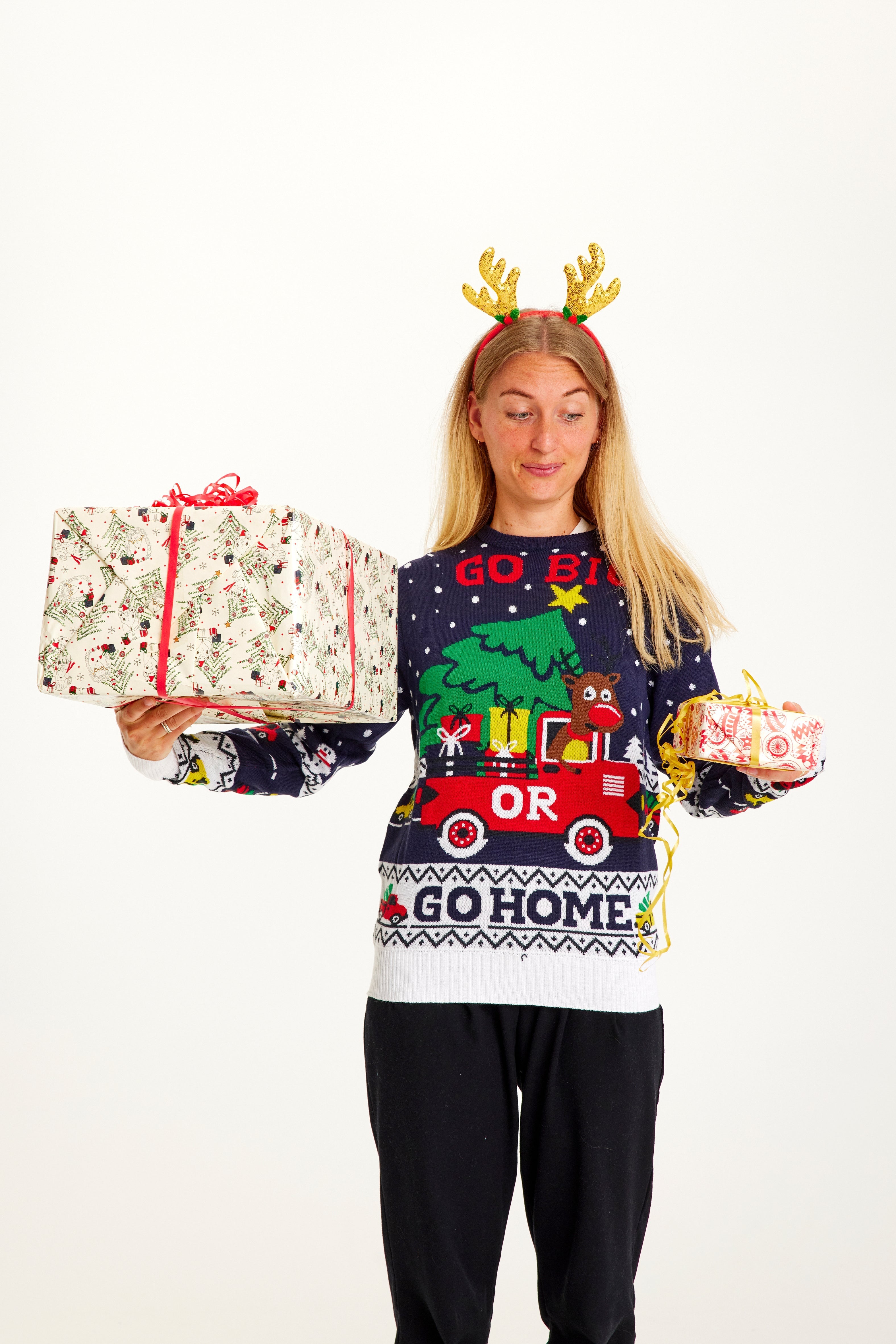 En kvinne som poserer med gaver i hendene, har på seg en blå julegenser med sitatet 