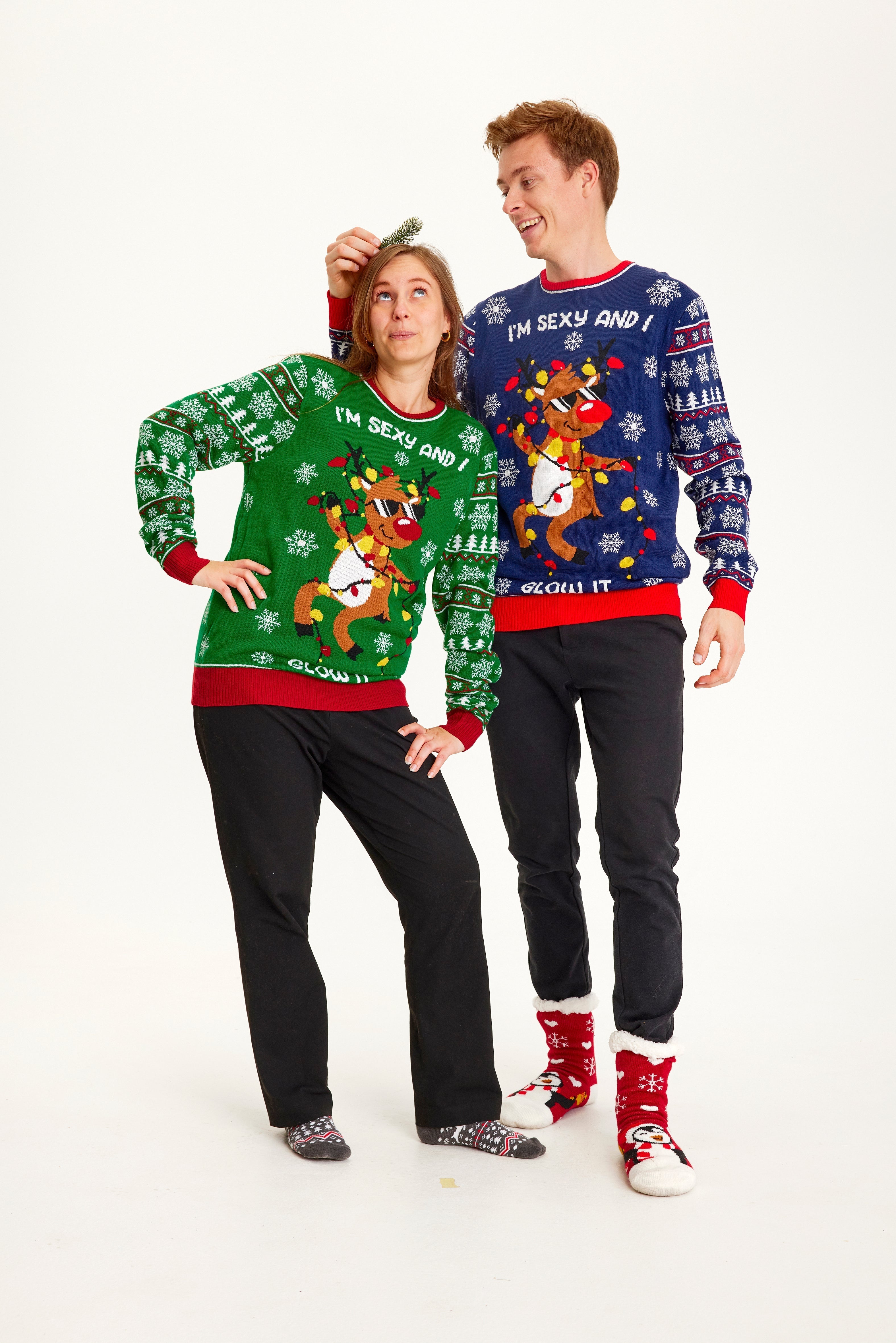 En mann og en kvinne iført julegenser med dansende reinsdyr og lys.