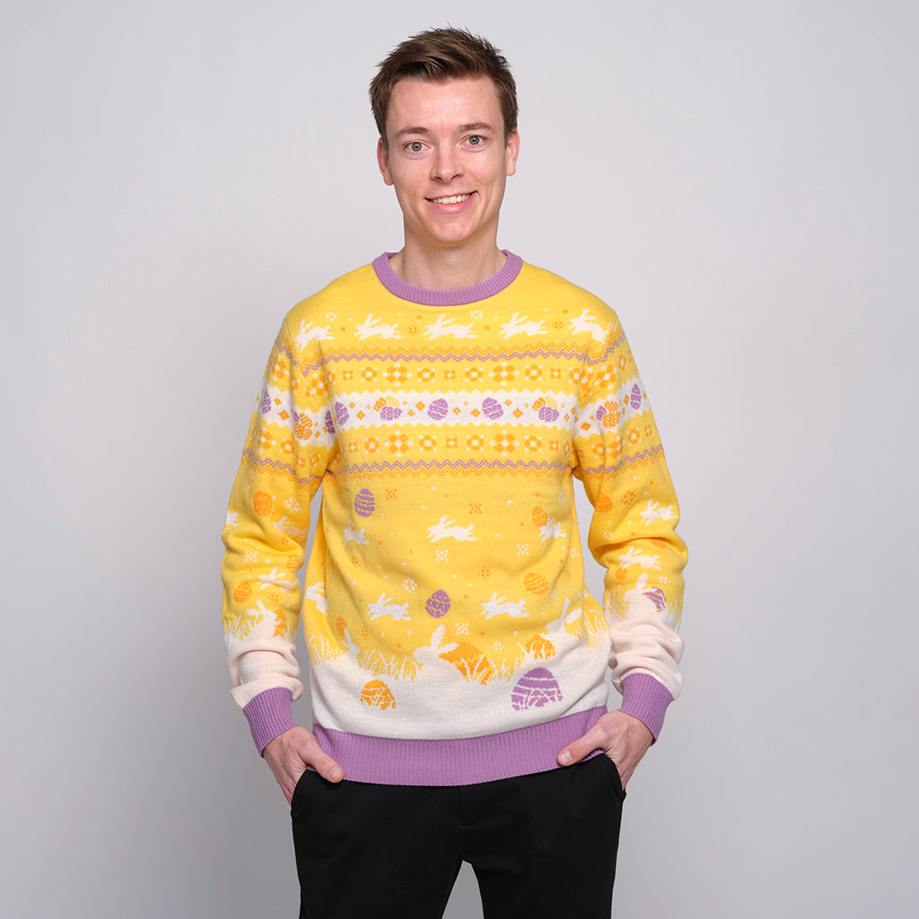 En smilende mann med hendene i lommene har på seg en gul påskegenser med harer på.