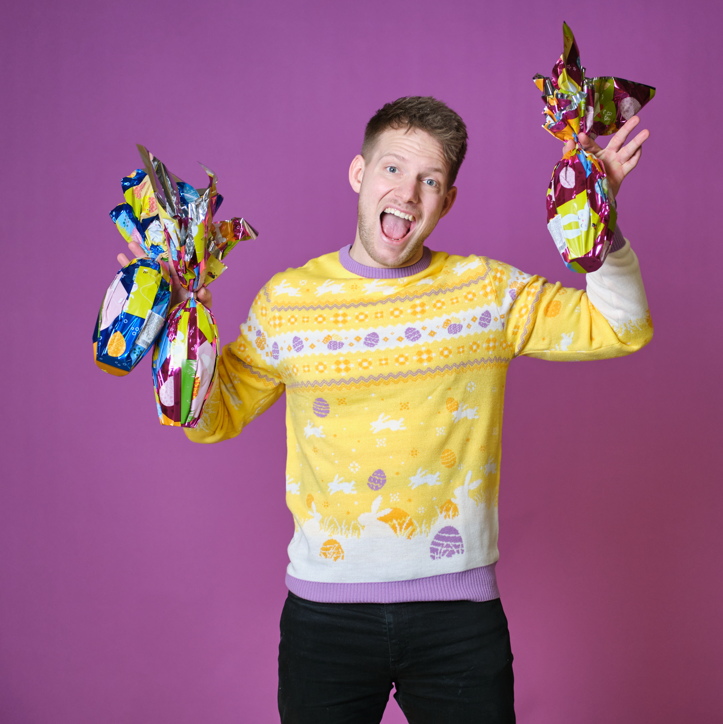 En smilende mann med sjokoladepåskeegg har på seg en gul påskegenser med harer på.